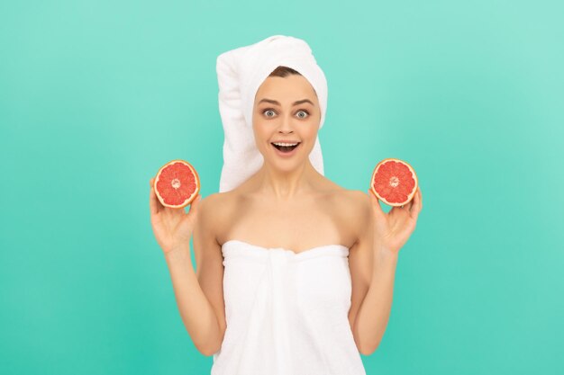 Jeune femme étonnée dans une serviette après la douche avec du pamplemousse sur fond bleu