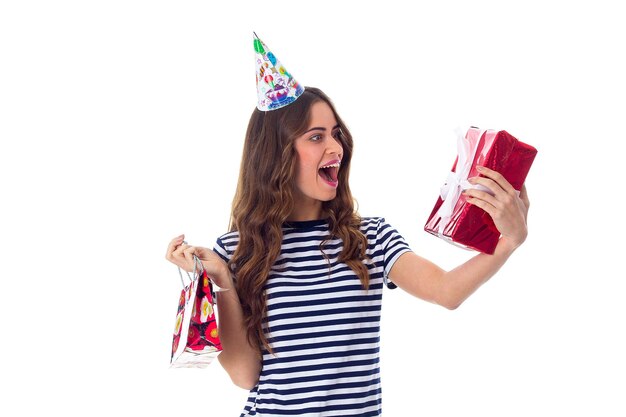 Jeune femme étonnée en T-shirt dépouillé et casquette de célébration tenant des cadeaux en studio