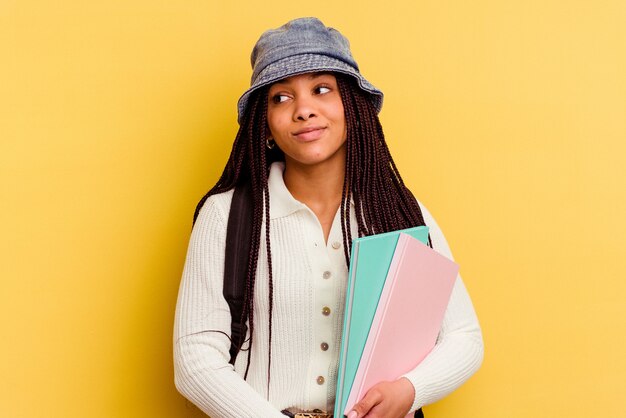 Jeune femme étudiante afro-américaine isolée sur jaune rêvant d'atteindre les objectifs et les buts