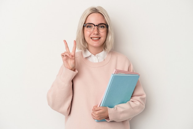 Jeune femme étudiante caucasienne tenant des livres isolés sur fond blanc montrant le numéro deux avec les doigts.