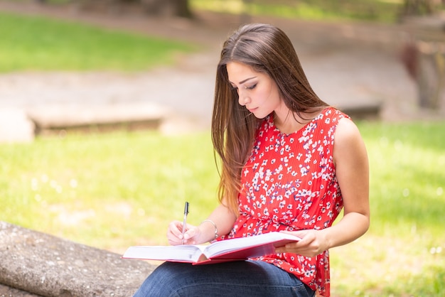 Jeune femme étudiante écrit sur un livre en plein air dans un parc