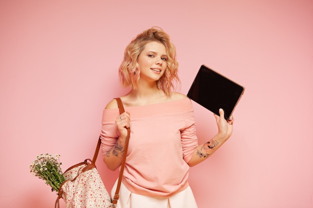 Photo jeune femme étudiante hipster souriante avec couleur rose bouclée coiffure et tatouage tenant la tablette
