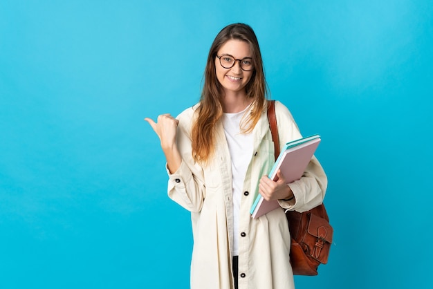 Jeune femme étudiante sur mur isolé pointant vers le côté pour présenter un produit