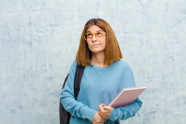 Jeune femme étudiante à la perplexité et confus, se demandant ou essayant de résoudre un problème ou en réfléchissant au mur de mur