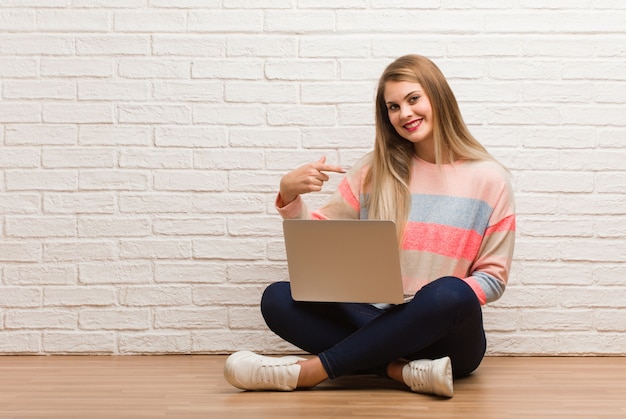 Jeune femme étudiante russe assis personne pointant à la main vers un espace de copie de chemise, fier et confiant