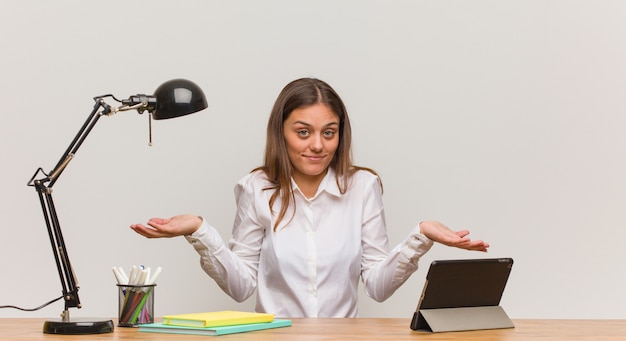 Jeune femme étudiante travaillant sur son bureau doutant et haussant les épaules