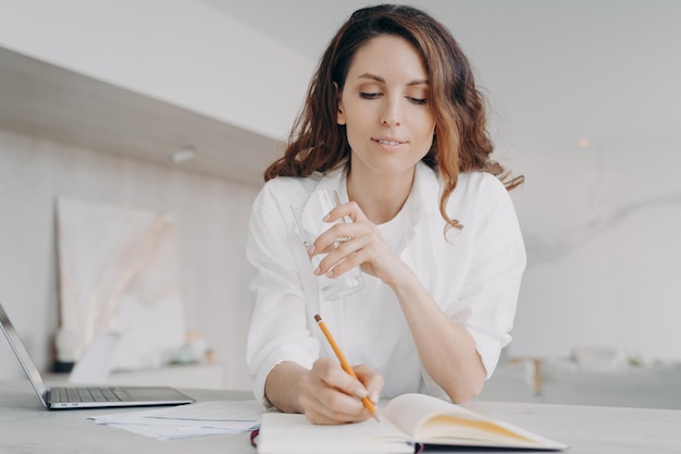 Jeune femme européenne en blanc prend des notes Bonne fille écrit dans un cahier