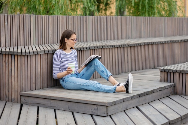 Une jeune femme européenne confiante se repose et lit un livre une femme boit du café se détend ou