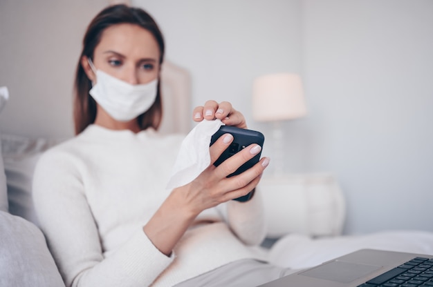 Jeune femme européenne dans un masque facial dans la chambre avec un ordinateur portable pendant l'isolement du coronavirus