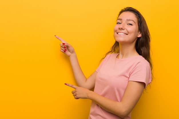 Jeune femme européenne isolée sur jaune excité pointant avec l'index loin.