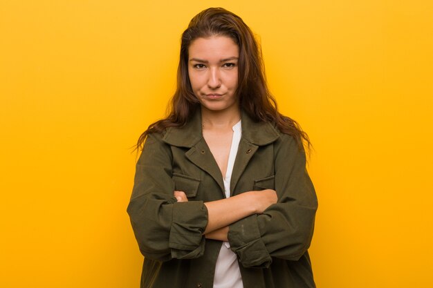 Jeune femme européenne isolée sur jaune fronçant les sourcils de mécontentement, garde les bras croisés.