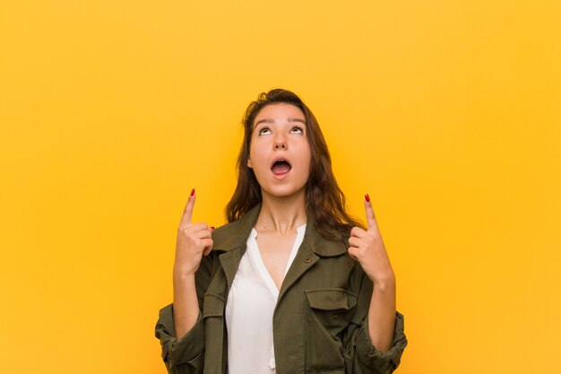 Jeune femme européenne isolée sur jaune pointant à l'envers avec la bouche ouverte.