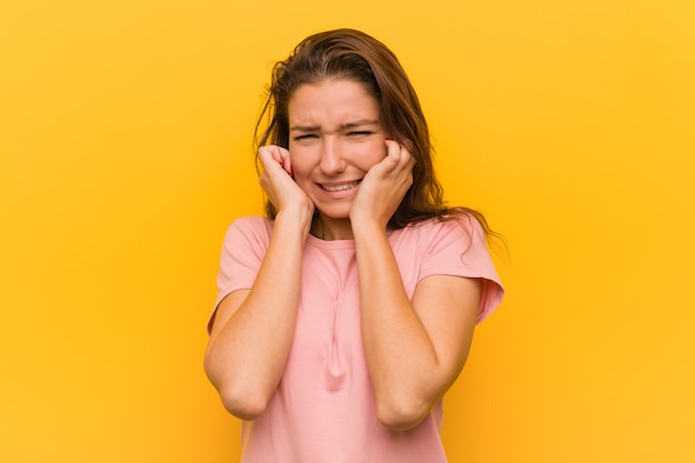 Jeune femme européenne isolée sur un mur jaune couvrant ses oreilles avec ses mains.