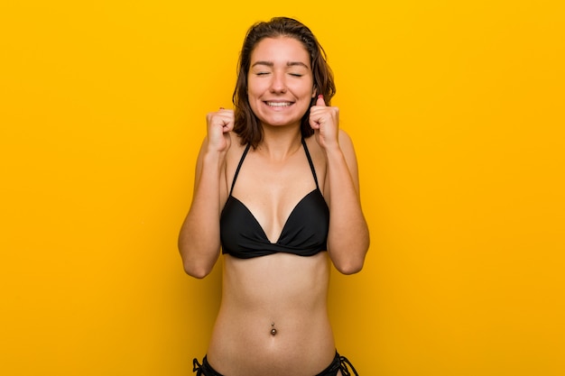 Photo jeune femme européenne portant un bikini levant le poing, se sentant heureuse et réussie. concept de victoire.