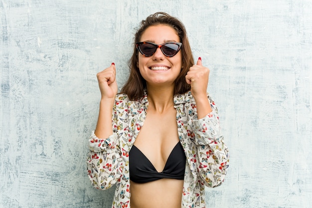 Jeune femme européenne portant un bikini levant le poing, se sentant heureuse et réussie. Concept de victoire.