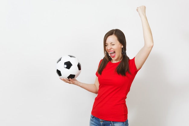 Jeune femme européenne ravie, deux queues de cheval amusantes, fan de football ou joueur en uniforme rouge tenant un ballon de football classique isolé sur fond blanc. Santé du football sportif, concept de mode de vie sain.