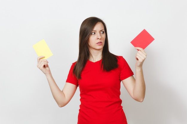 Une jeune femme européenne sérieuse et sévère, l'arbitre de football tient à choisir des cartes de football jaunes et rouges, propose au joueur de se retirer du terrain isolé sur fond blanc. Sport, jeu, concept de mode de vie sain.