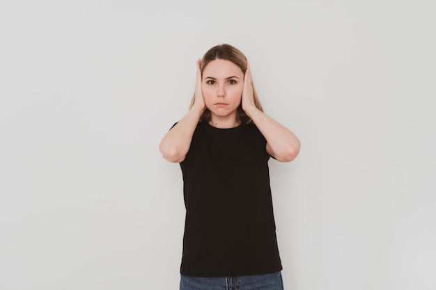 Jeune femme européenne en t-shirt noir tenant son visage avec des paumes sur fond blanc