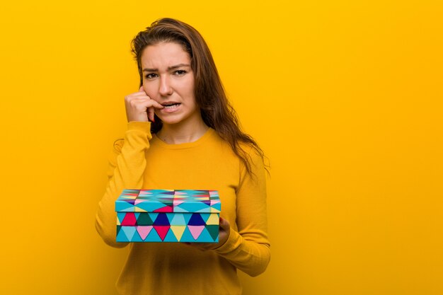 Jeune femme européenne tenant un cadeau se ronger les ongles, nerveux et très anxieux.