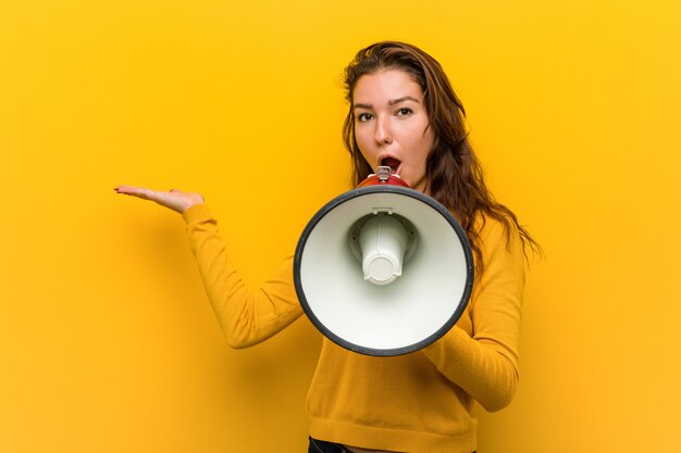 Jeune femme européenne tenant un mégaphone impressionné tenant copie sur la paume.