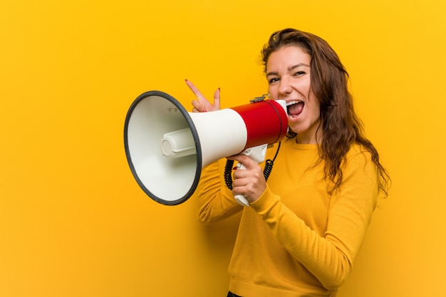 Jeune femme européenne tenant un mégaphone souriant gaiement pointant avec l'index.