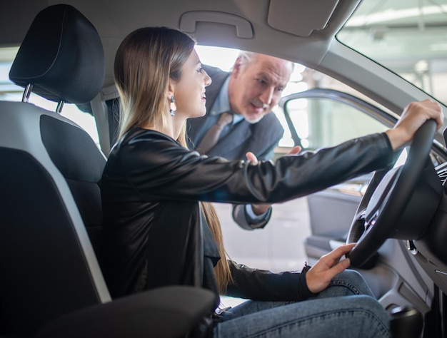 Une jeune femme examinant une nouvelle voiture dans un concessionnaire automobile d'exposition explique ses caractéristiques