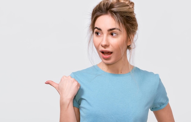 Jeune femme excitée européenne portant un t-shirt bleu décontracté indiquant un espace de copie vierge pour le texte publicitaire regardant de côté posant sur fond de studio gris Émotions des gens