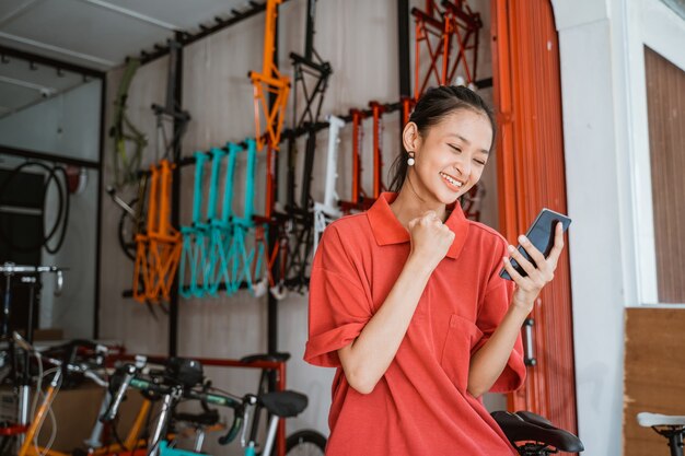 Jeune femme excitée avec les mains serrées en regardant sur l'écran du smartphone