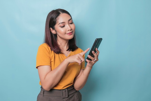 Une jeune femme excitée pointant son smartphone dans sa main isolée sur fond bleu