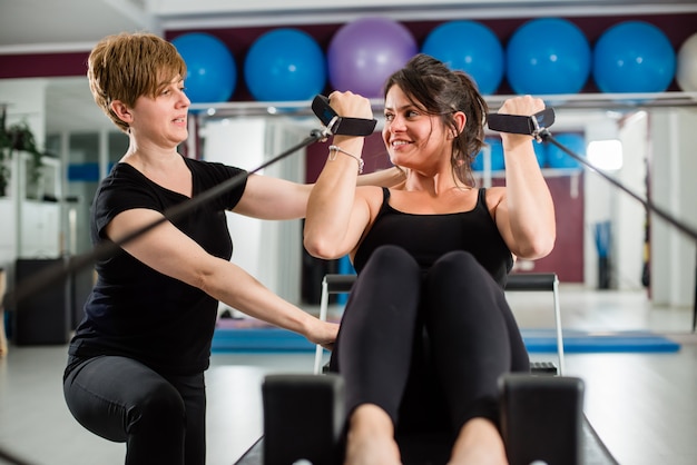 Jeune femme, exercice, sur, pilates, appareil, reformer, à, instructeur, à, gymnase