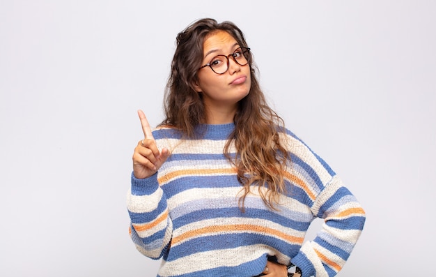 jeune femme expressive avec des lunettes posant sur un mur blanc