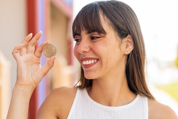 Jeune femme à l'extérieur tenant un Bitcoin et le regardant