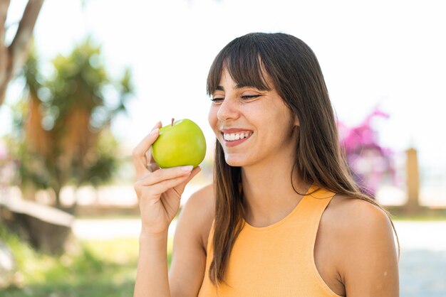 Une jeune femme à l'extérieur tenant une pomme avec une expression heureuse