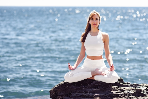 Jeune femme, faire du yoga sur la plage, porter des vêtements blancs