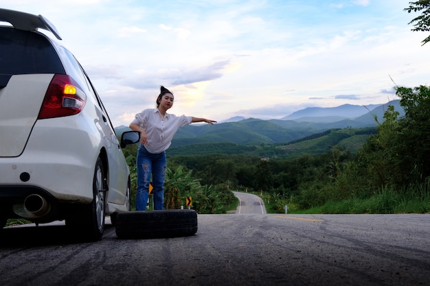 Jeune femme faisant de l'auto-stop sur la route sur la voie publique dans la zone forestière au fond de la montagne et du ciel