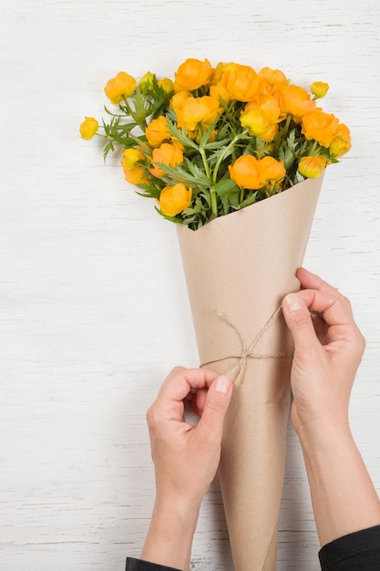 Jeune femme faisant un bouquet de fleurs jaunes sur fond de bois blanc