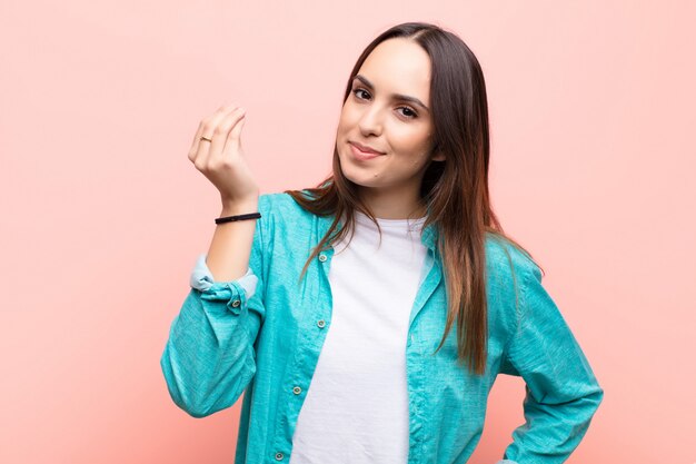 Jeune femme faisant capice ou geste d'argent, vous disant de payer vos dettes! sur le mur rose