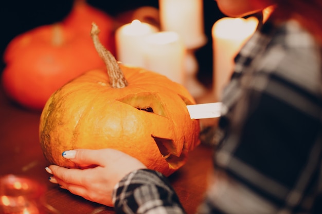 Jeune femme faisant la citrouille d'Halloween Jack-o-lantern avec des bougies. Mains femelles coupant des potirons avec le couteau