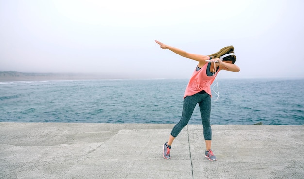 Jeune femme faisant de la danse dab en plein air par la jetée de la mer