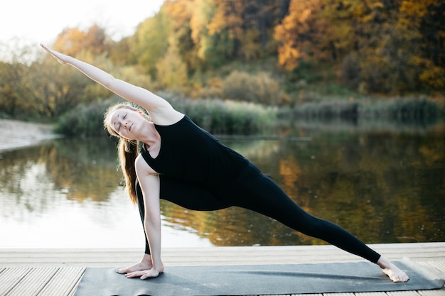 Jeune femme faisant du yoga asana dans la nature près du lac