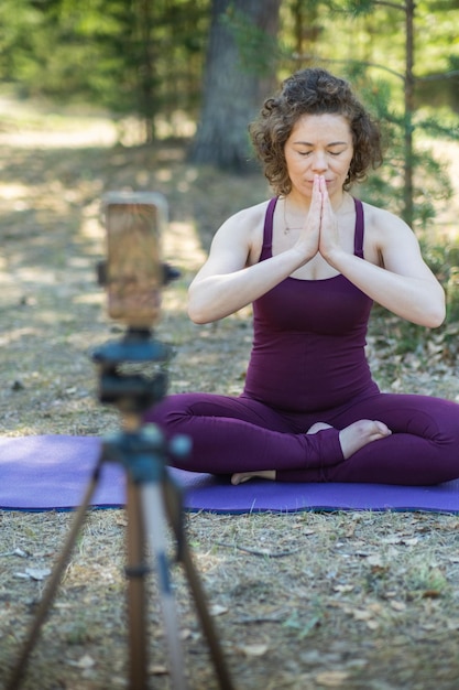 Photo une jeune femme faisant du yoga dans la nature en ligne en utilisant un téléphone et une application