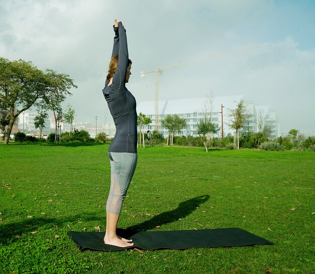 Jeune femme faisant du yoga, des étirements, de l'exercice, de l'entraînement dans le parc à l'aide de tapis de yoga. Yoga pour débutant naturel posant. Concept de soins de santé.