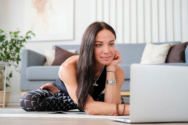 Jeune femme faisant du yoga à la maison devant un ordinateur portable