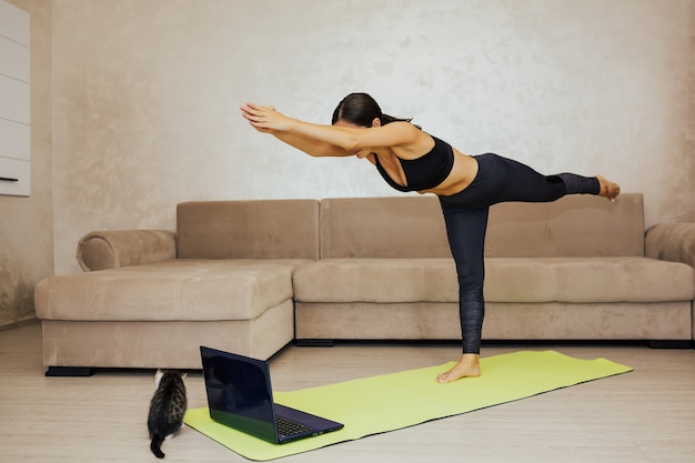 Jeune femme faisant du yoga à la maison. Elle pratique le yoga, fait de l'exercice Warrior III, pose Virabhadrasana 3