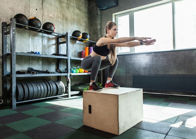 Jeune femme faisant un exercice de saut de boîte. Fit woman doing box squat au gymnase. Entraînement croisé