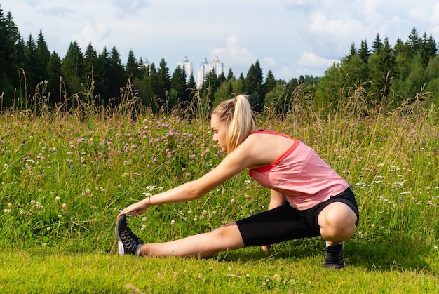 Jeune femme faisant des exercices d'étirement à l'extérieur dans un pré à l'extérieur de la ville