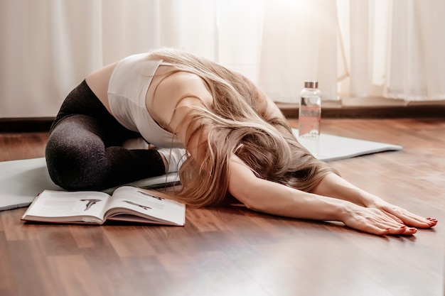 Jeune femme faisant des exercices de Pilates assis sur un tapis de yoga sur le sol à la maison. Sports d'étirement. Yoga à la maison