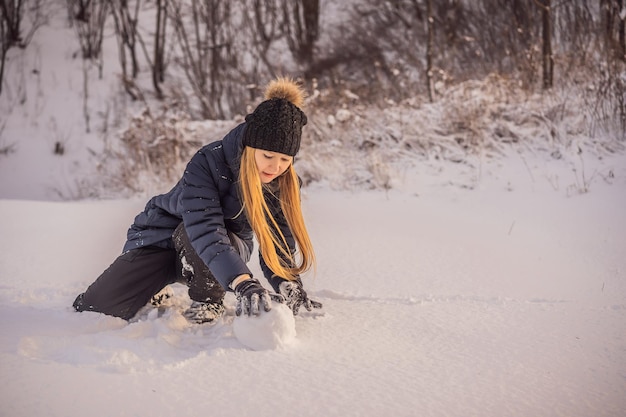 Jeune femme faisant rouler une boule de neige géante pour faire un bonhomme de neige