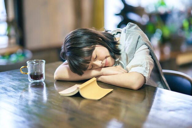 Une jeune femme faisant la sieste dans une pièce modérément lumineuse avec un livre et un verre de café