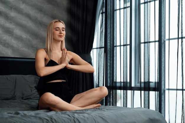 Une jeune femme fait du yoga et de la méditation le matin dans sa chambre à coucher, apprécie la solitude et pratique des poses méditatives.